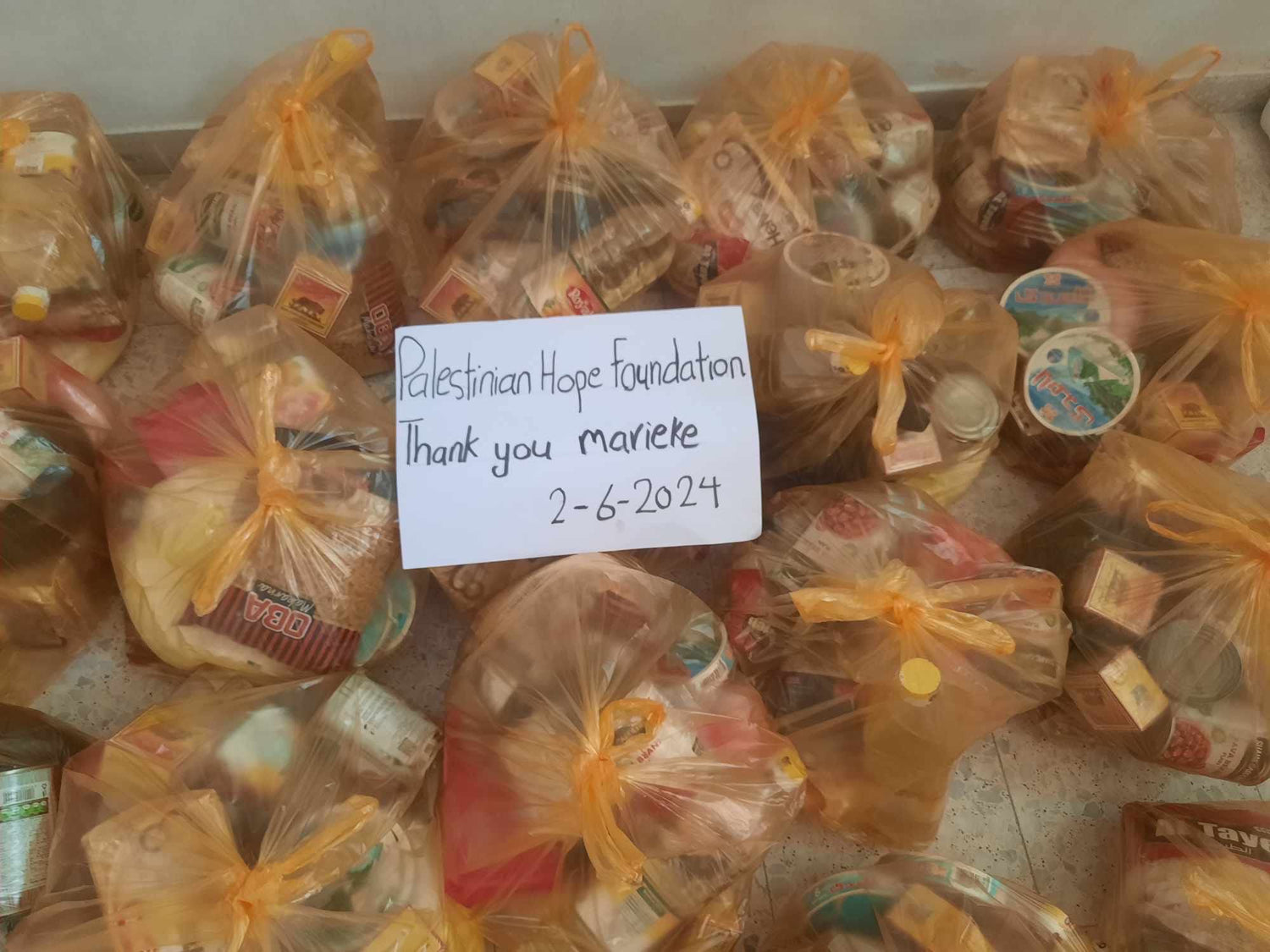 Voedselpakketten met een bord waarop staat 'Palestinian Hope Foundation - Thank you Marieke 2-6-2024', klaar om uitgedeeld te worden aan Palestijnse gezinnen in nood.